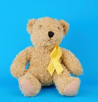 brown teddy bear sits and holds in his paw a yellow silk ribbon on a blue background photo