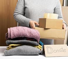 mujer en un suéter gris está empacando ropa en una caja, el concepto de asistencia y voluntariado foto