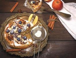 baked round apple pie and iron sieve with powdered sugar photo