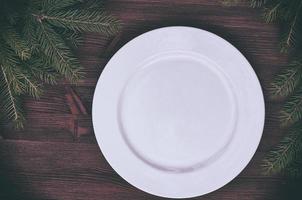 White empty plate with a green branch of spruce on a wooden surface photo