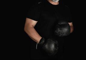 un joven se para en un estante de boxeo, usando guantes de boxeo negros muy antiguos foto