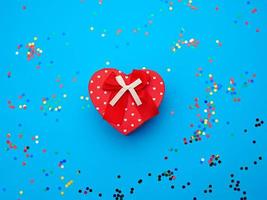 closed red heart-shaped cardboard box on a blue background with multi-colored shiny confetti photo