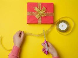 las manos femeninas están cortando una cinta de seda con tijeras, junto a cajas de regalo. fondo amarillo, vista superior foto