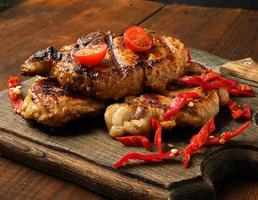 trozos de carne de cerdo a la parrilla en una parrilla sobre una tabla de madera vintage foto