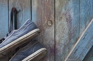 pair of old dirty and worn blue sneakers hang on a nail