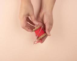 two hands hold a wooden bobbin with red wool threads photo