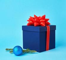 square blue cardboard box with a red bow, sprig of spruce with a shiny blue ball photo