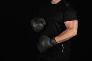 young man stands in a boxing rack, wearing very old vintage black boxing gloves photo