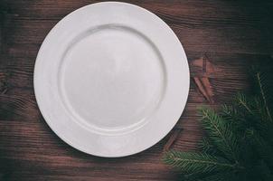 White empty plate with a green branch of spruce on a wooden surface photo