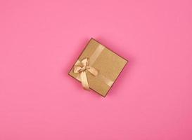 caja de regalo dorada cerrada con un lazo en un fondo rosa foto