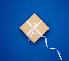 cardboard gift square box tied with a white thin ribbon on a dark blue background photo