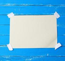A4 blank white sheet attached with adhesive tape to a blue wooden surface photo