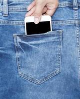 female hand holds a white phone in the back of the blue jeans photo