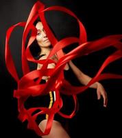 young woman gymnast of Caucasian appearance with black hair spins red satin ribbons photo