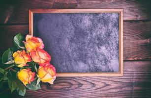 black wooden frame next to a bouquet of yellow roses photo