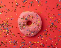 one pink round donut with colored sprinkles on a red background photo