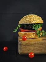 Tasty burger with fried cutlet and grilled vegetables served on a wooden board with cherry tomatoes photo