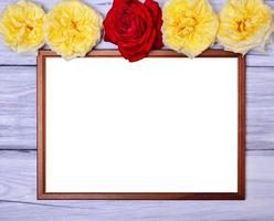 Empty wooden frame on a white wooden background, at the top of the buds of flowering roses photo