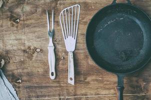 Empty black cast-iron frying pan with vintage kitchen items on a brown table photo