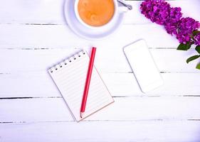 Empty little notebook with a red pencil and a mobile phone on a white wooden surface photo