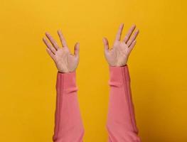 two female hands in a pink sweater are raised in the air, palms are open. Yellow background photo