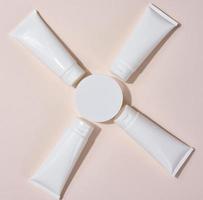 White plastic tubes, jars and other form of packaging for cosmetics on a beige background, top view. Template for branding, advertising and product promotion photo