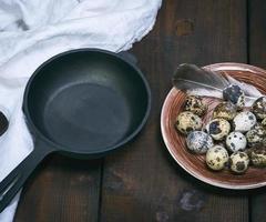 empty round cast-iron frying pan and raw quail eggs in a plate photo