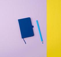 closed notebook and wooden blue pencil on a colored background photo