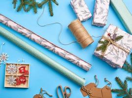 rolls with wrapping paper, brown rope, scissors, decor and a wrapped square box with a gift photo