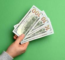 female hand holding a stack of paper one hundred dollar bills on a green background photo