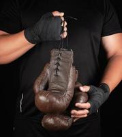 athlete in black clothes holds very old vintage leather brown boxing gloves photo