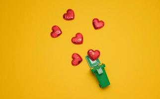 red hearts and a miniature plastic box for collecting garbage on a yellow background photo