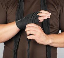 man wraps his hands in black textile bandage for sports, white background photo