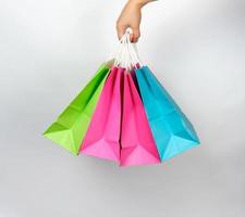mano femenina sosteniendo cuatro bolsas de embalaje de compras de papel de colores foto