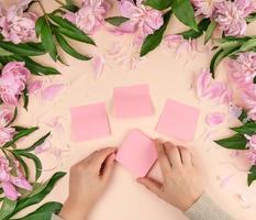 female hands glue empty paper pink stickers on the background with blooming peonies