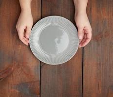 hands hold empty gray round ceramic plate, wooden background photo