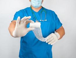 médico masculino con uniforme azul y guantes de látex con venda de gasa estéril blanca foto