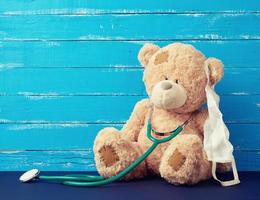 teddy bear is sitting in a white medical mask, green stethoscope is hanging on his neck photo