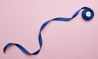 curled blue satin ribbon on pink background, flat lay photo