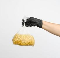 female hand in a black glove holds a transparent bag with raw fusilli pasta photo