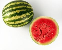 half ripe watermelon with red juicy pulp and seeds and a whole green photo