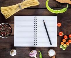 cuaderno en blanco con hojas blancas, pasta larga cruda e ingredientes para cocinar foto