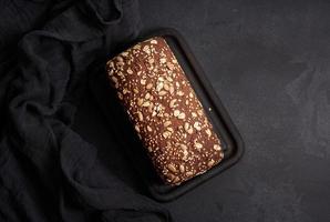 baked square rye flour bread with oatmeal on black background, top view photo