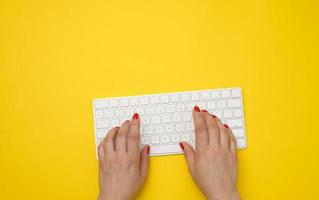 dos manos femeninas presionan teclas en un teclado inalámbrico blanco, mesa amarilla foto