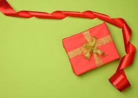 red gift box tied with a silk ribbon on the green background, top view photo