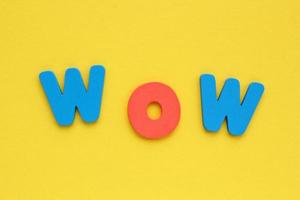 Word WOW colored letters on yellow background. Positive, happy, fun concept. Flatlay, top view photo