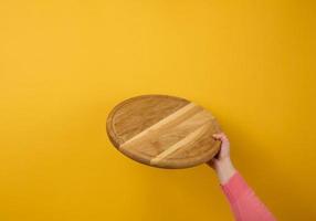 woman holding empty round wooden pizza board in hand, body part  ona  yellow background
