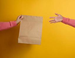 mujer sosteniendo en la mano una bolsa de papel artesanal marrón en blanco para llevar sobre fondo amarillo. maqueta de plantilla de embalaje. concepto de servicio de entrega foto