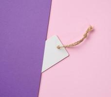 Empty white paper tag on a rope, pink background. Price template, top view photo