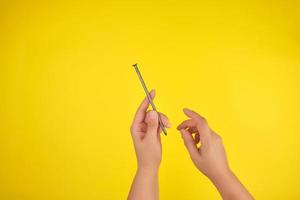 two female hands hold a large iron nail, yellow background, photo